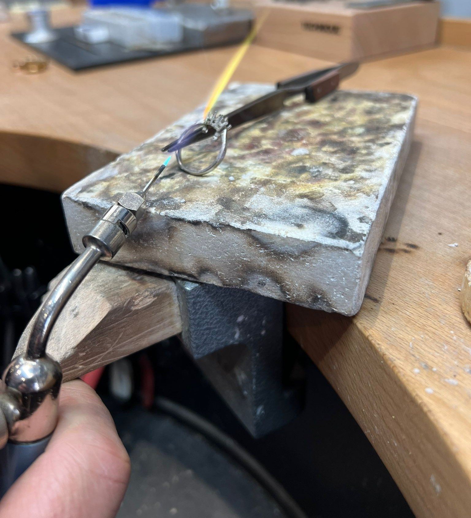 A ring on a firestone block on the workshop bench at Toulson Jones Jewellers, soldering torch and steel file in frame