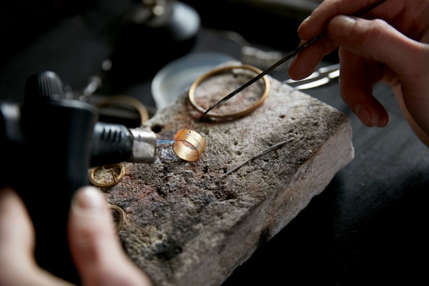Two yellow-gold rings on a firestone block, soldering torch in hand at the Toulson Jones workshop